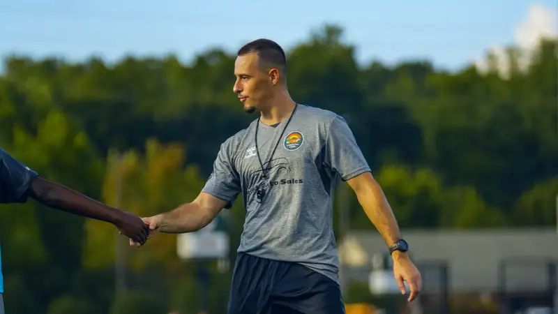A CCFC coach in a grey staff top shaking hands with a player at the end of a training session
