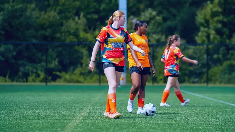 Three CCFC players in orange and red kit walking the ball up the pitch during a league match