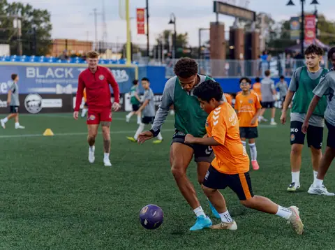 A young player in an orange bib shielding the ball from a player in green during a small-sided game