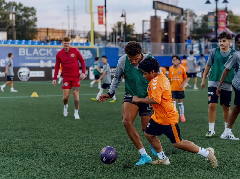 A young player in an orange bib shielding the ball from a player in green during a small-sided game