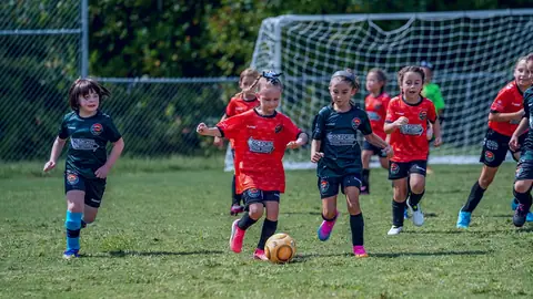 U7 Players in orange and green CCFC jerseys chase after the ball