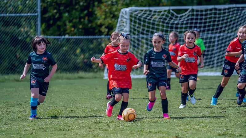 U7 Players in orange and green CCFC jerseys chase after the ball