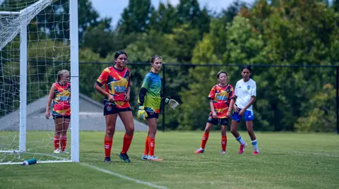 A CCFC girls' team in orange and yellow kit lined up beside the goal during a tournament match