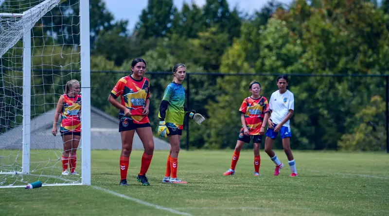 A CCFC girls' team in orange and yellow kit lined up beside the goal during a tournament match